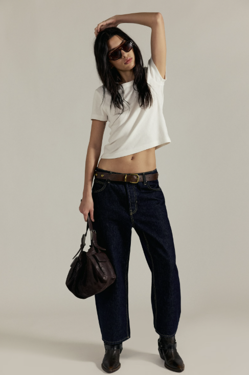 Woman wearing a white t-shirt, dark jeans, and sunglasses on a plain background