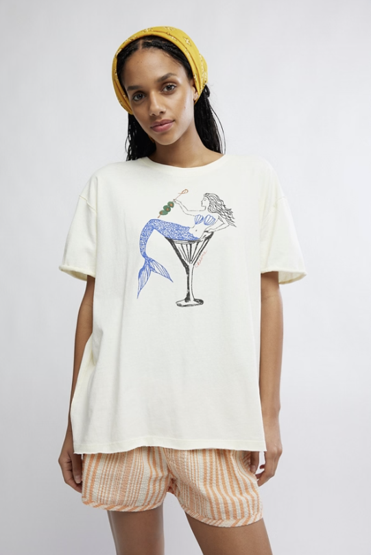 Woman wearing white graphic tee with mermaid in martini glass on plain background