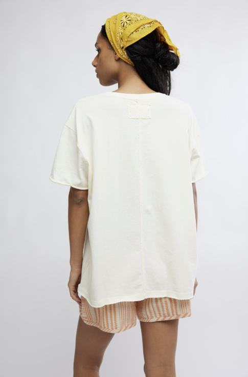Woman wearing a white oversized shirt and striped shorts with a yellow headscarf on a plain background
