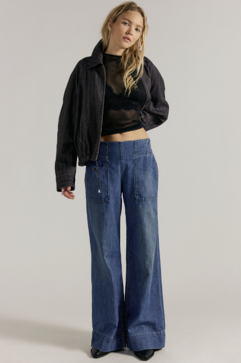 Woman wearing black jacket and shirt with medium wash wide leg denim jeans on plain background