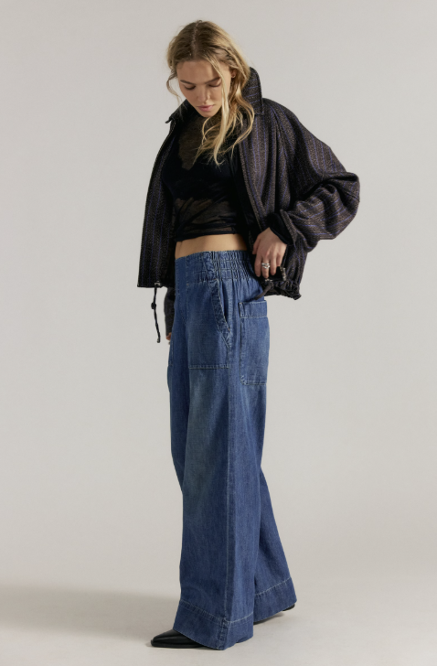 Woman wearing black jacket and shirt with medium wash wide leg jeans on plain background