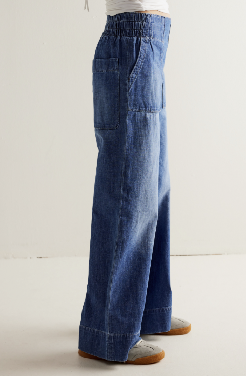 Woman shown from side view waist down wearing medium wash wide leg denim jeans on plain background
