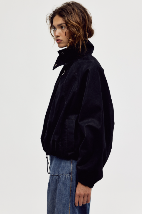 Woman shown from side view wearing black suede jacket and jeans on plain background