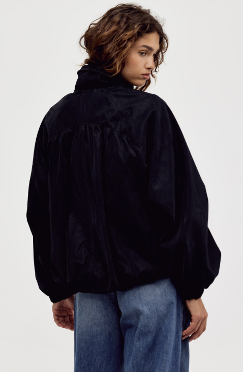 Woman shown from back view wearing black suede jacket and jeans on plain background