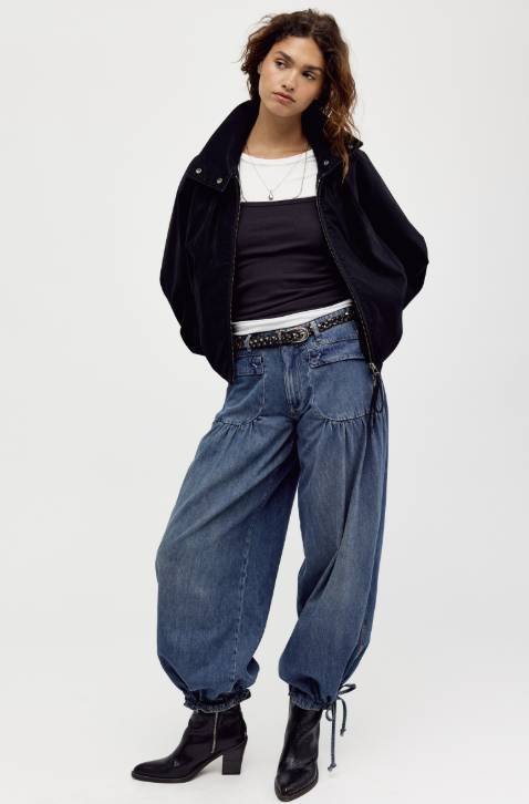 Woman wearing black suede jacket with black and white undershirt and jeans on plain background