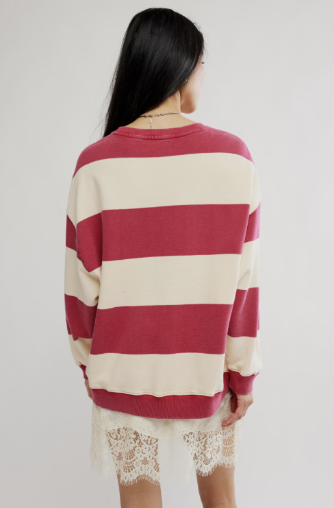 A woman shown from behind wearing a cream and red striped crewneck sweater, paired with a white lace skirt, against a plain light gray background.
