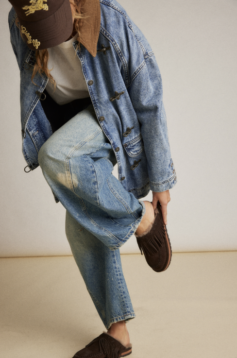 Person wearing denim putting on brown suede fringe mule in studio setting