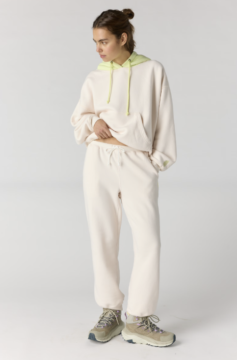 Woman wearing matching cream hoodie and joggers with lime hood on plain background