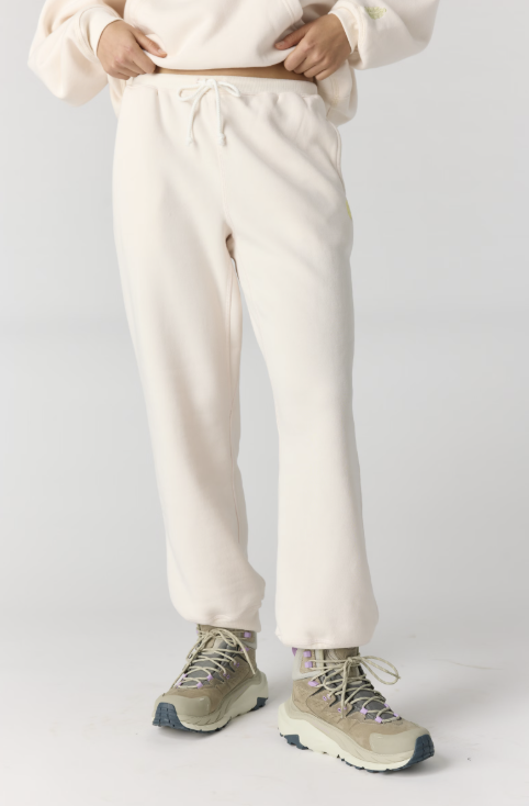 Woman shown waist down wearing cream colored joggers on plain background