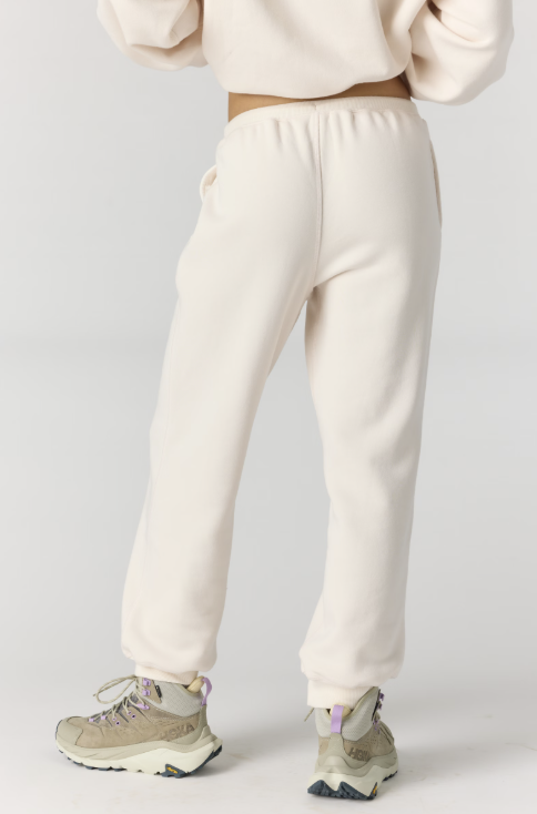 Woman shown from back view wearing cream color joggers and matching hoodie on plain background