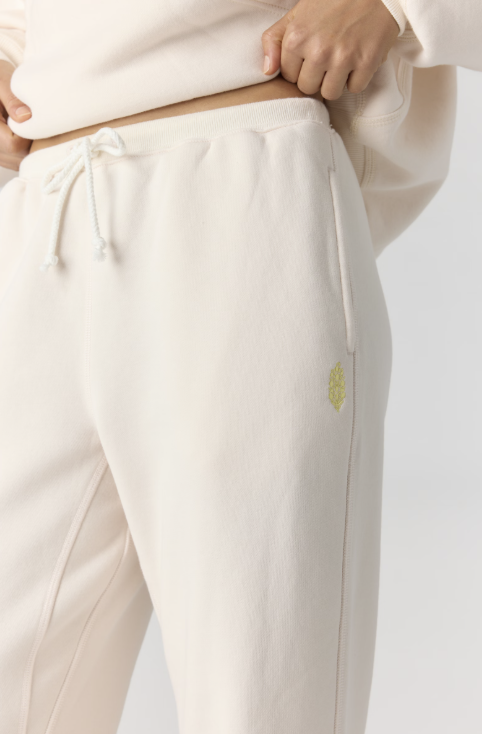 Close up of cream color joggers with yellow logo on pocket on plain background
