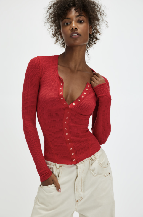Woman wearing red front snap cardigan with beige pants on plain background
