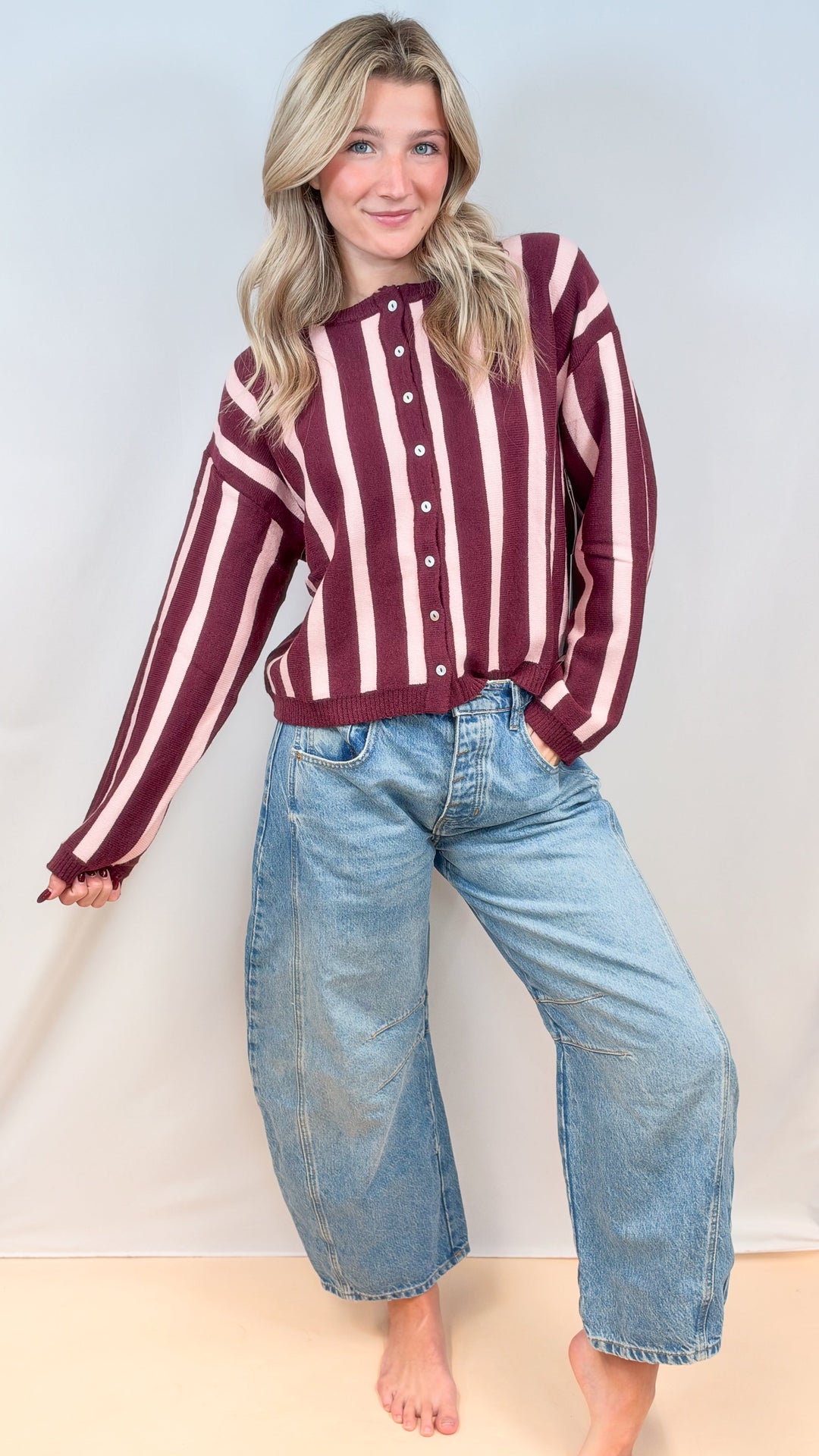 Woman wearing burgundy and pink stripe cardigan with jeans on plain background