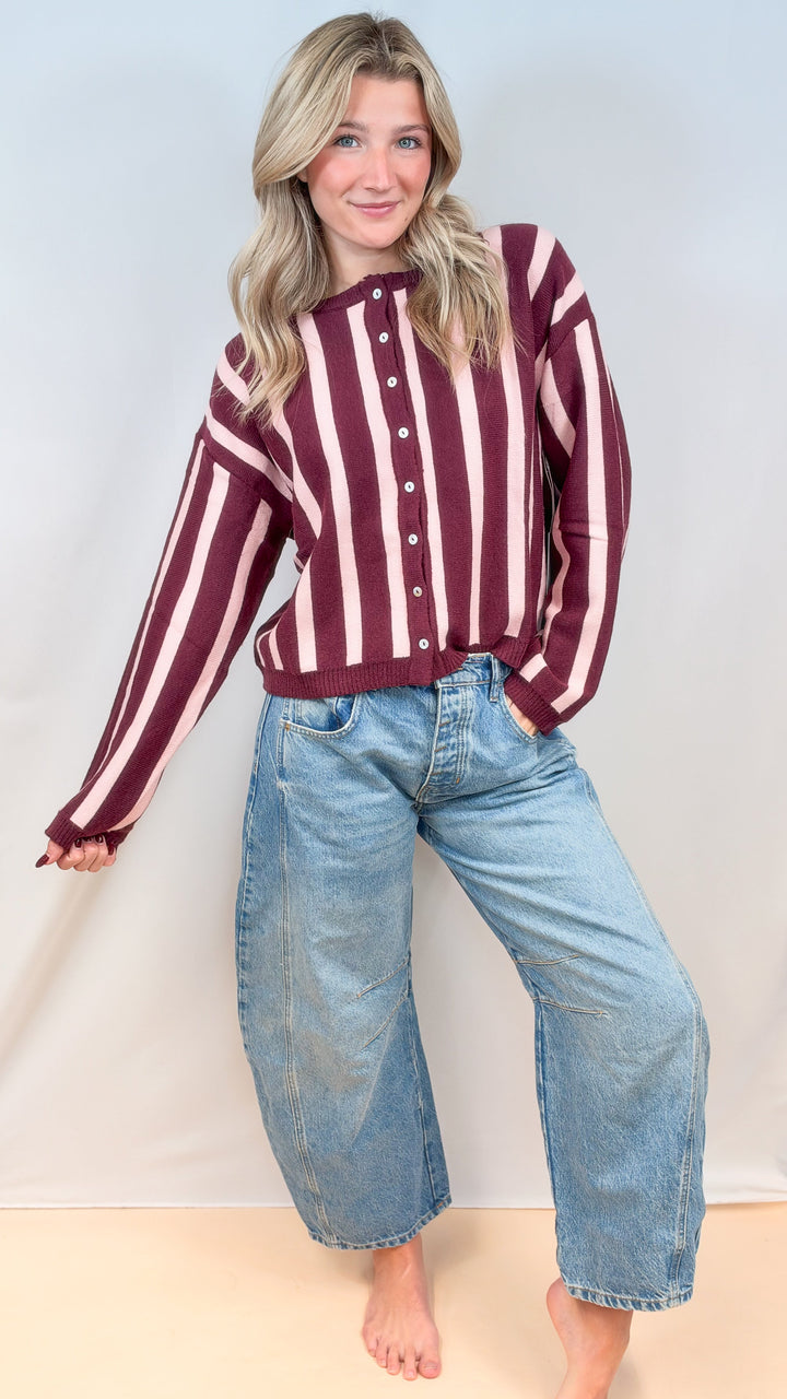 Woman wearing burgundy and pink stripe cardigan with jeans on plain background