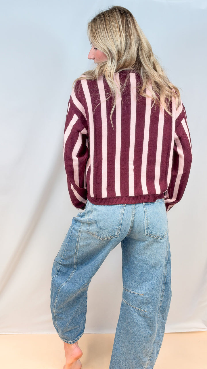 Woman shown from back wearing burgundy and pink stripe top with barrel jeans on plain background
