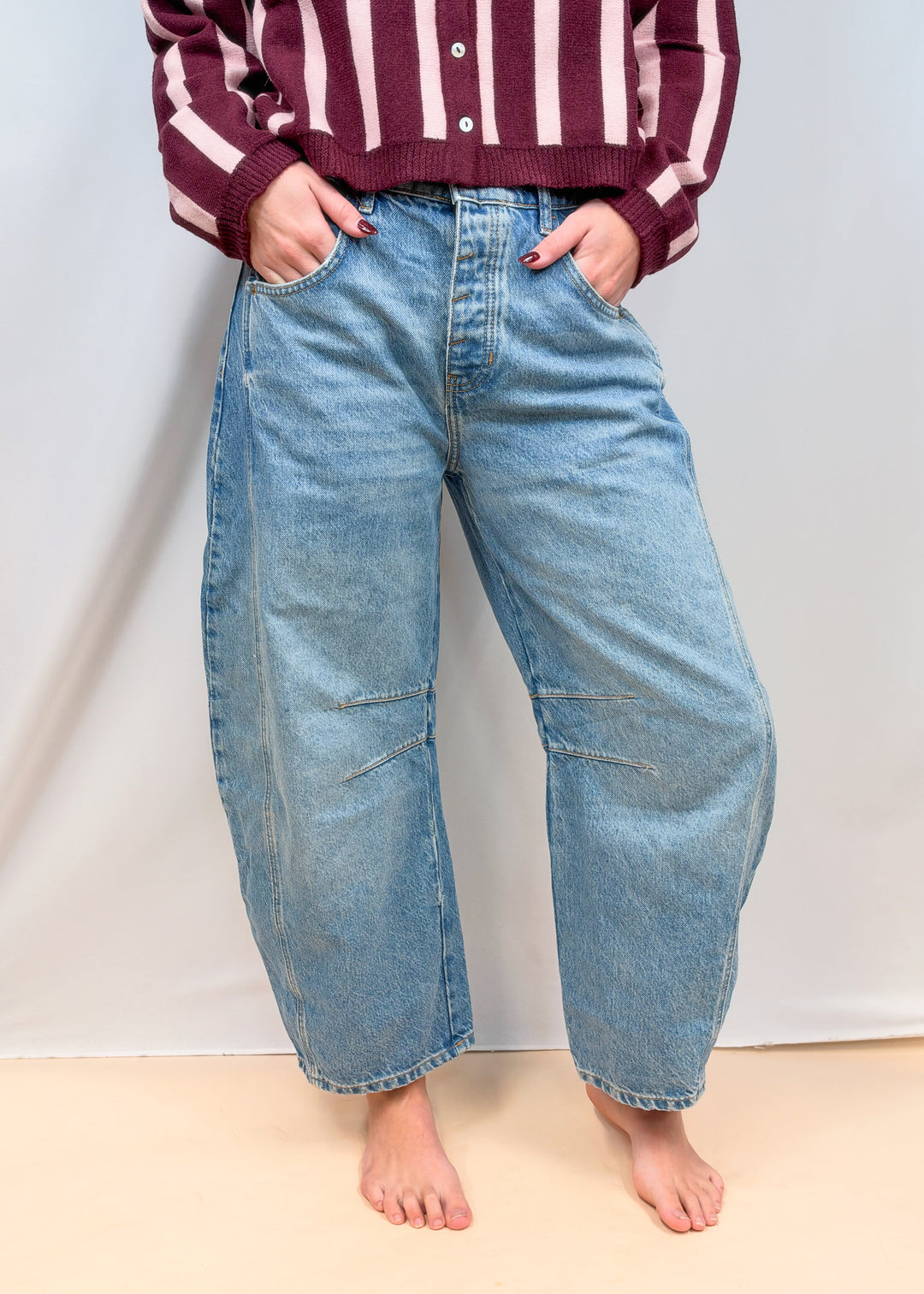 Woman shown waist down wearing barrel jeans on plain background