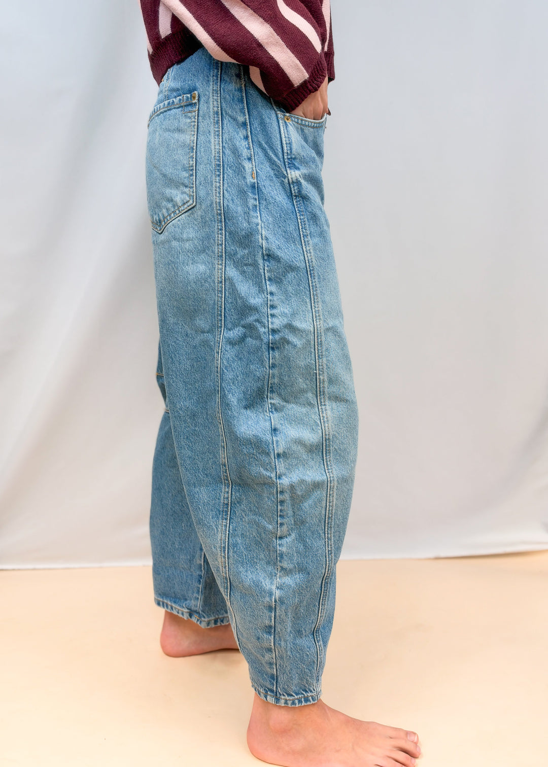 Woman shown from side view wearing barrel jeans on plain background