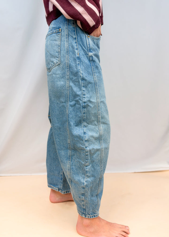 Woman shown from side view wearing barrel jeans on plain background