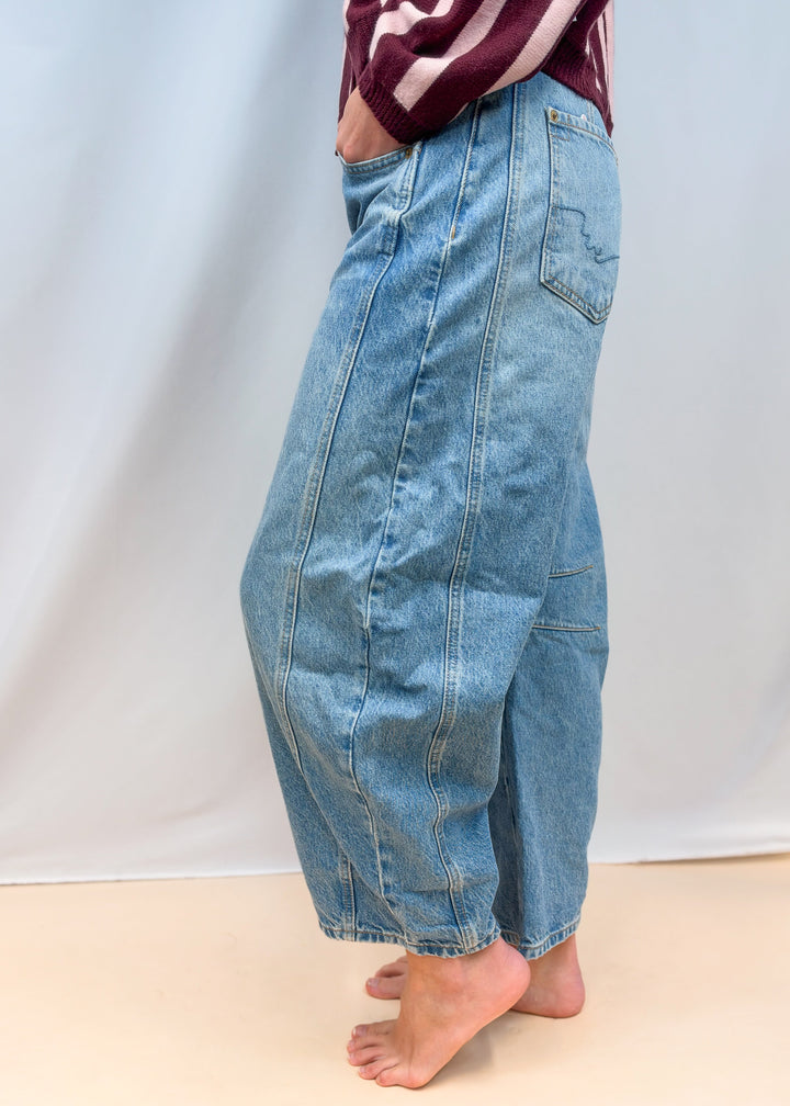 Woman shown from side view waist down wearing barrel jeans on plain background