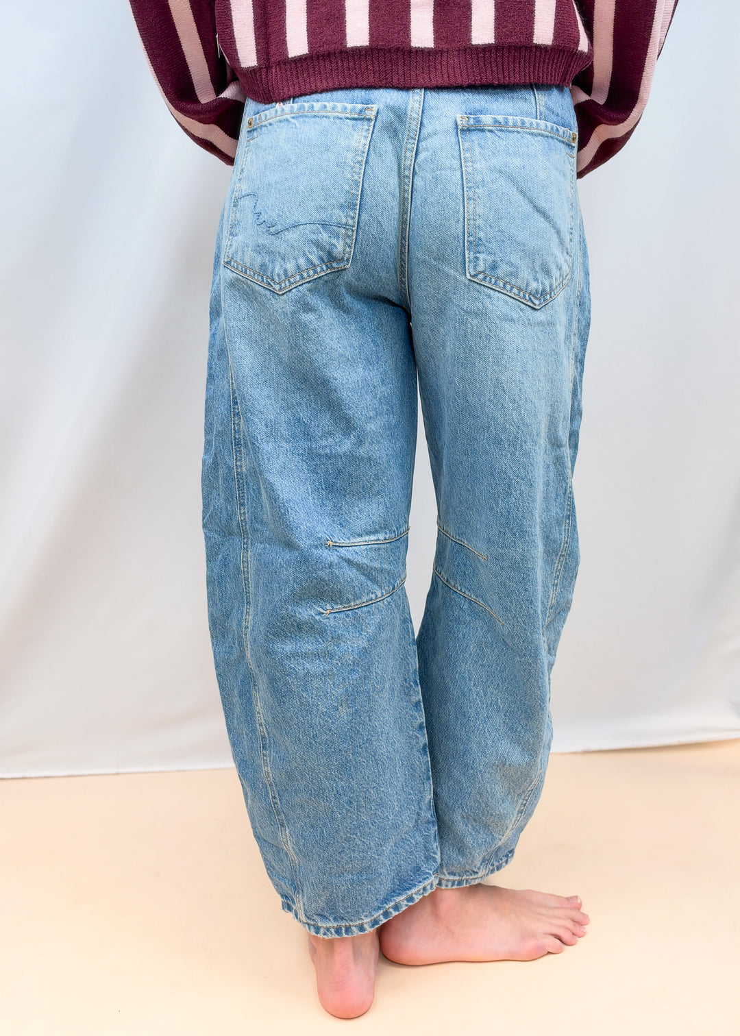 Woman shown from back view waist down wearing barrel jeans on plain background