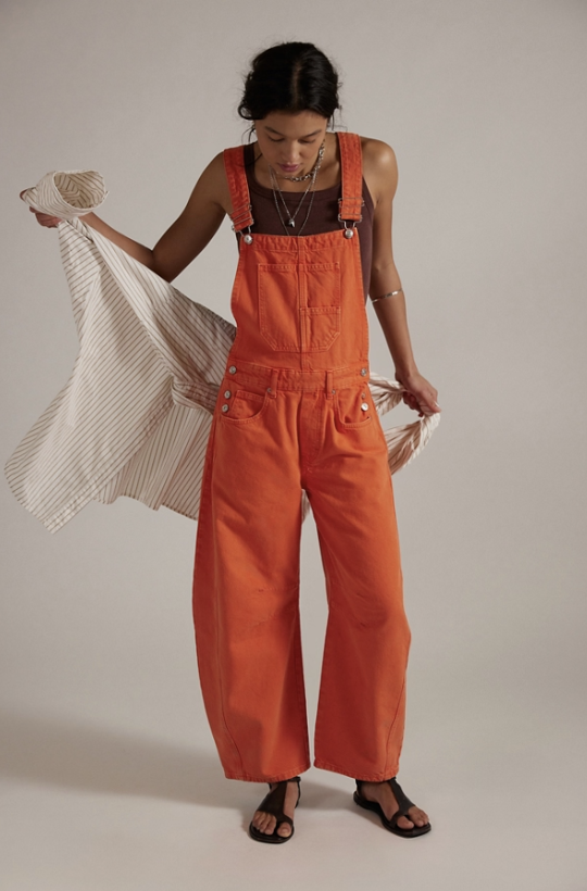 Person wearing orange overalls holding a striped bag against a plain background