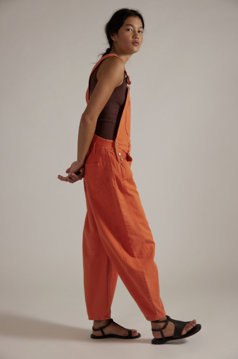 Woman wearing orange overalls with brown tank on plain background