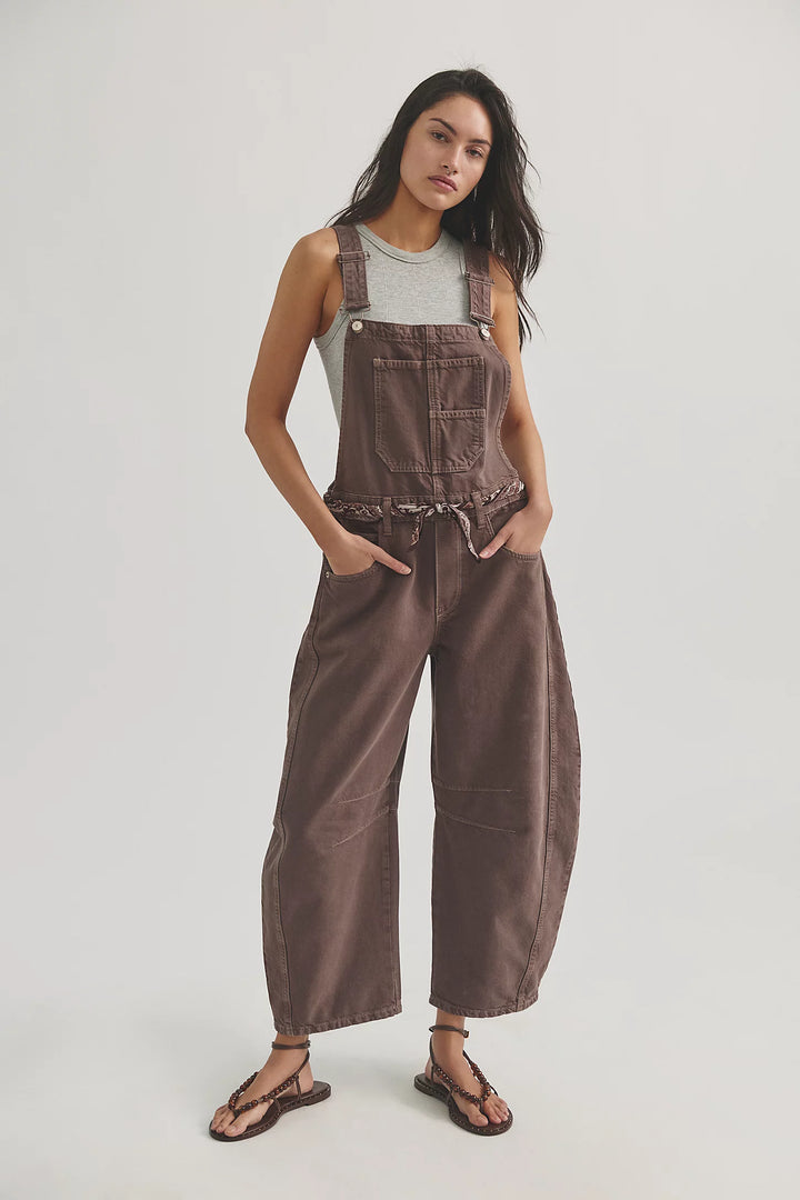 Woman wearing brown overalls with grey tank and scarf belt on plain background