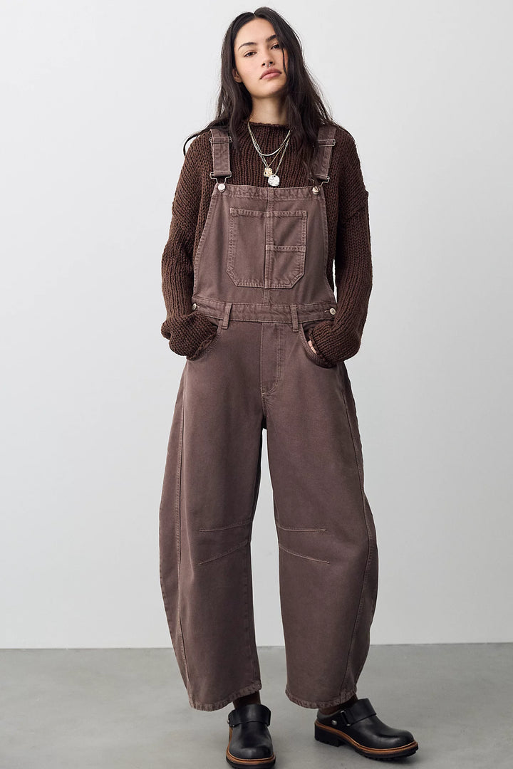Woman wearing brown barrel overalls with brown sweater on plain background