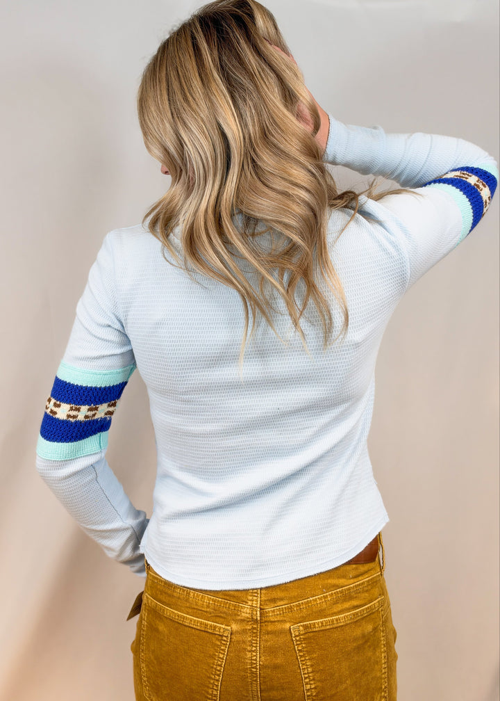 Woman shown from back view wearing light blue top and camel color cord pants on plain background