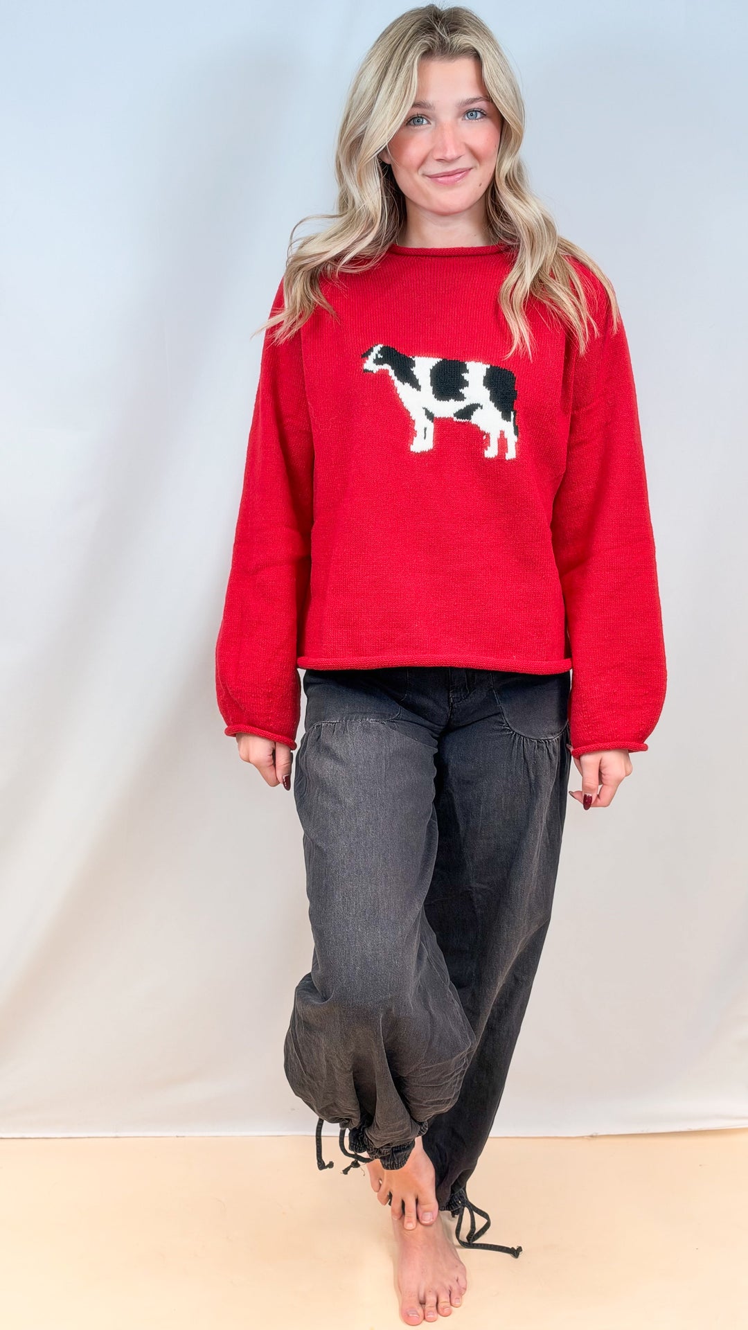 Woman wearing red sweater with cow design and black balloon pants on plain background