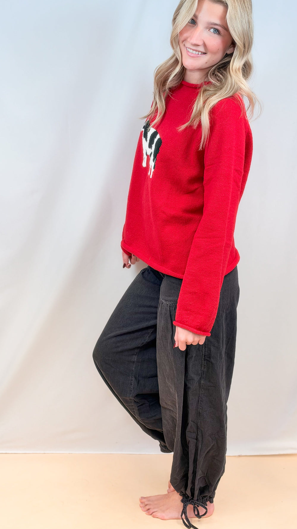 Woman shown from side view wearing red sweater and black balloon pants on plain background