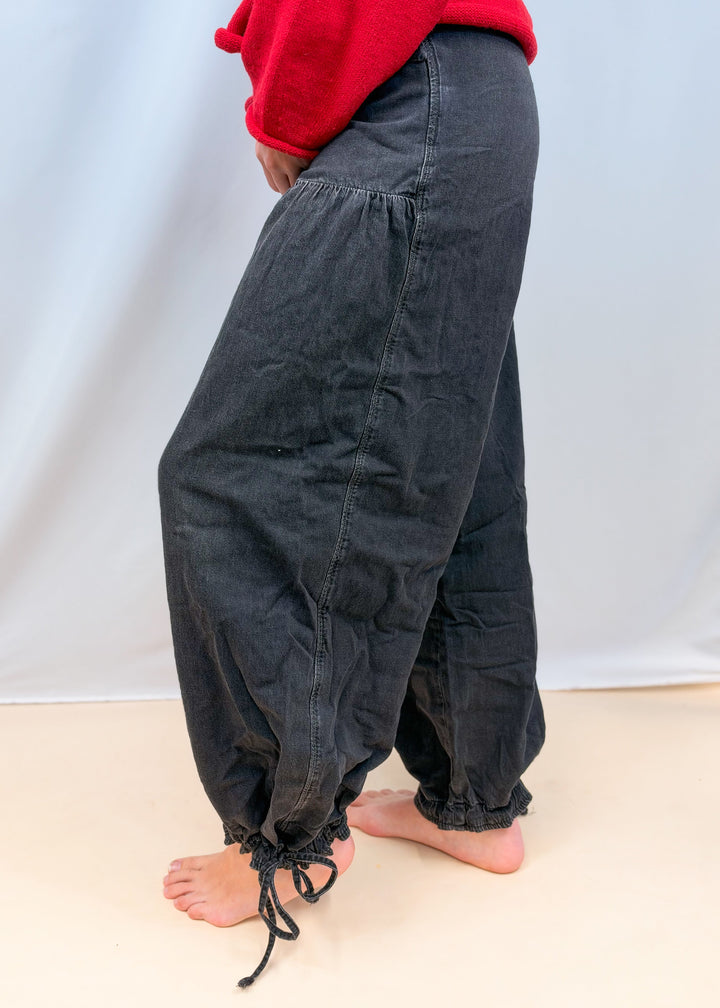 Woman shown from side view wearing black balloon pants on plain background