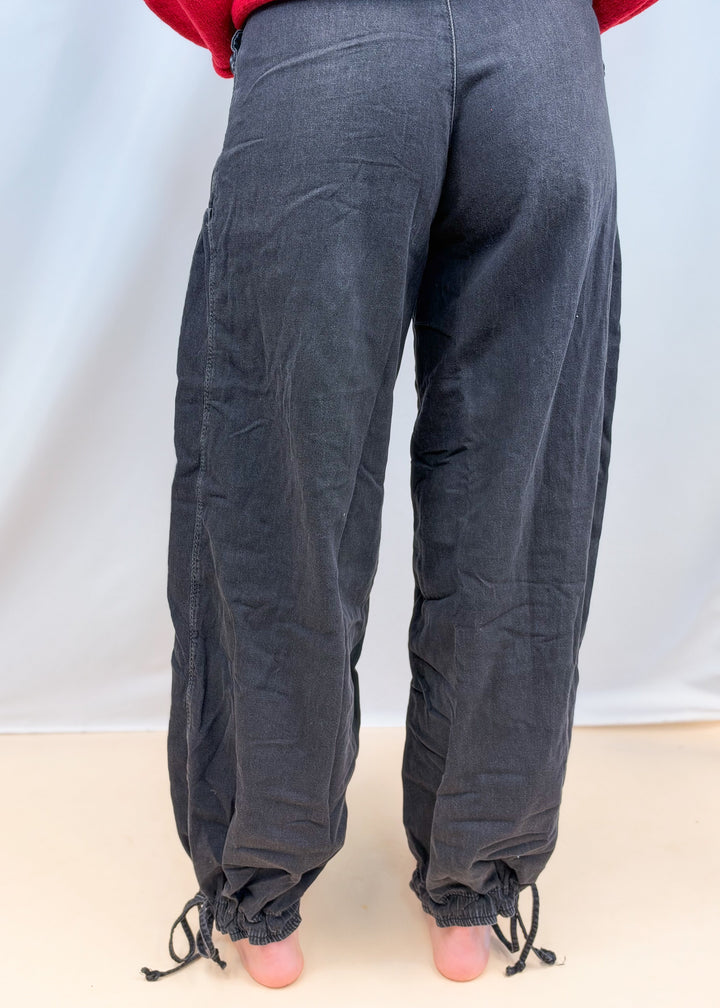 Woman shown from back view wearing black balloon pants on plain background