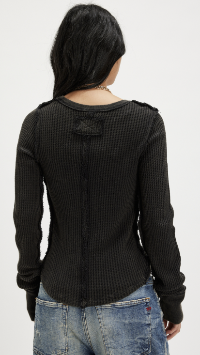 Woman shown from back wearing black long sleeve shirt and jeans on plain background