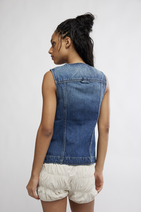 Person wearing a denim vest and white shorts on a plain background