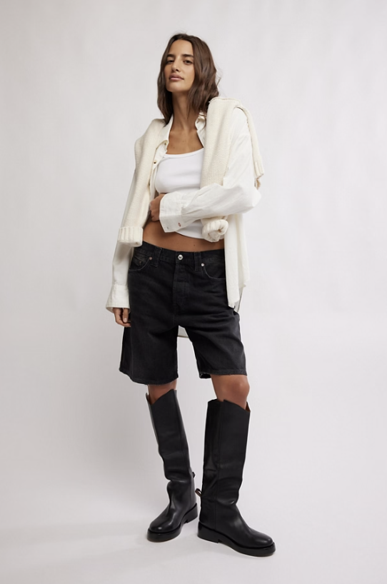 Woman wearing black denim shorts and white top on plain background