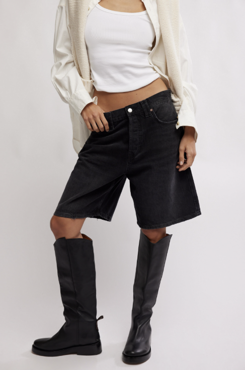 Person wearing black denim shorts and black knee-high boots on a white background