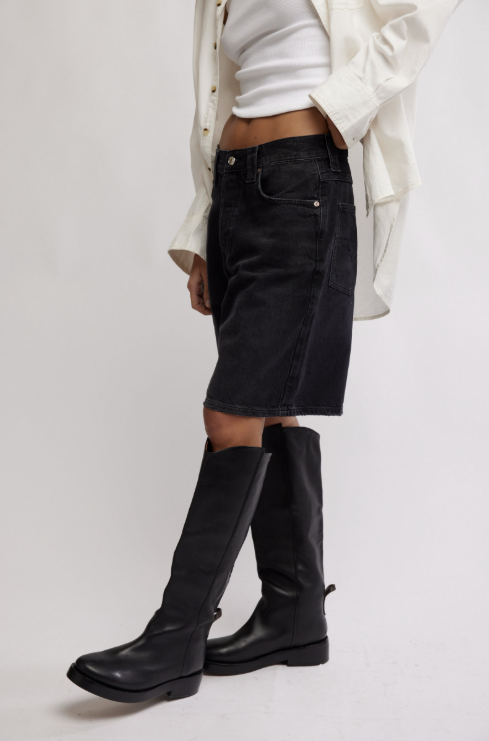 Person wearing black knee-high boots, black shorts, and a white jacket on a light gray background