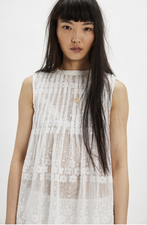 Woman wearing white mesh tunic and shorts on plain background