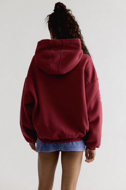 Woman shown from back view wearing red hooded sweatshirt and blue skirt on plain background
