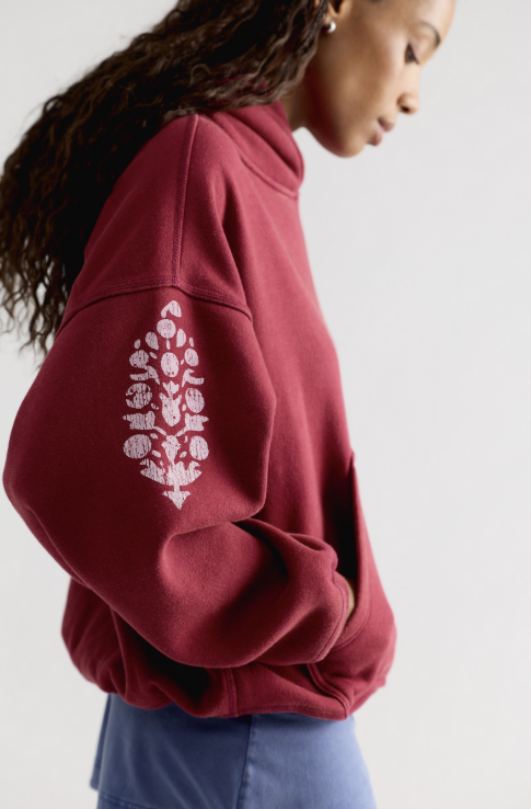 Close up of woman wearing red sweatshirt with logo on sleeve and blue skirt on plain background