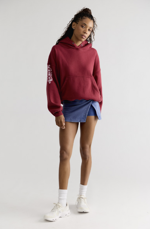 Woman wearing red sweatshirt with logo on sleeve with blue skirt on plain background