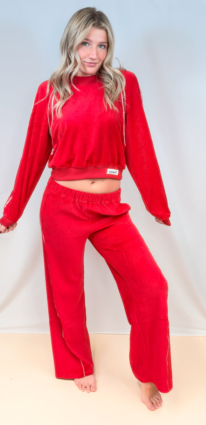 Woman wearing matching red velour set with white piping on plain background