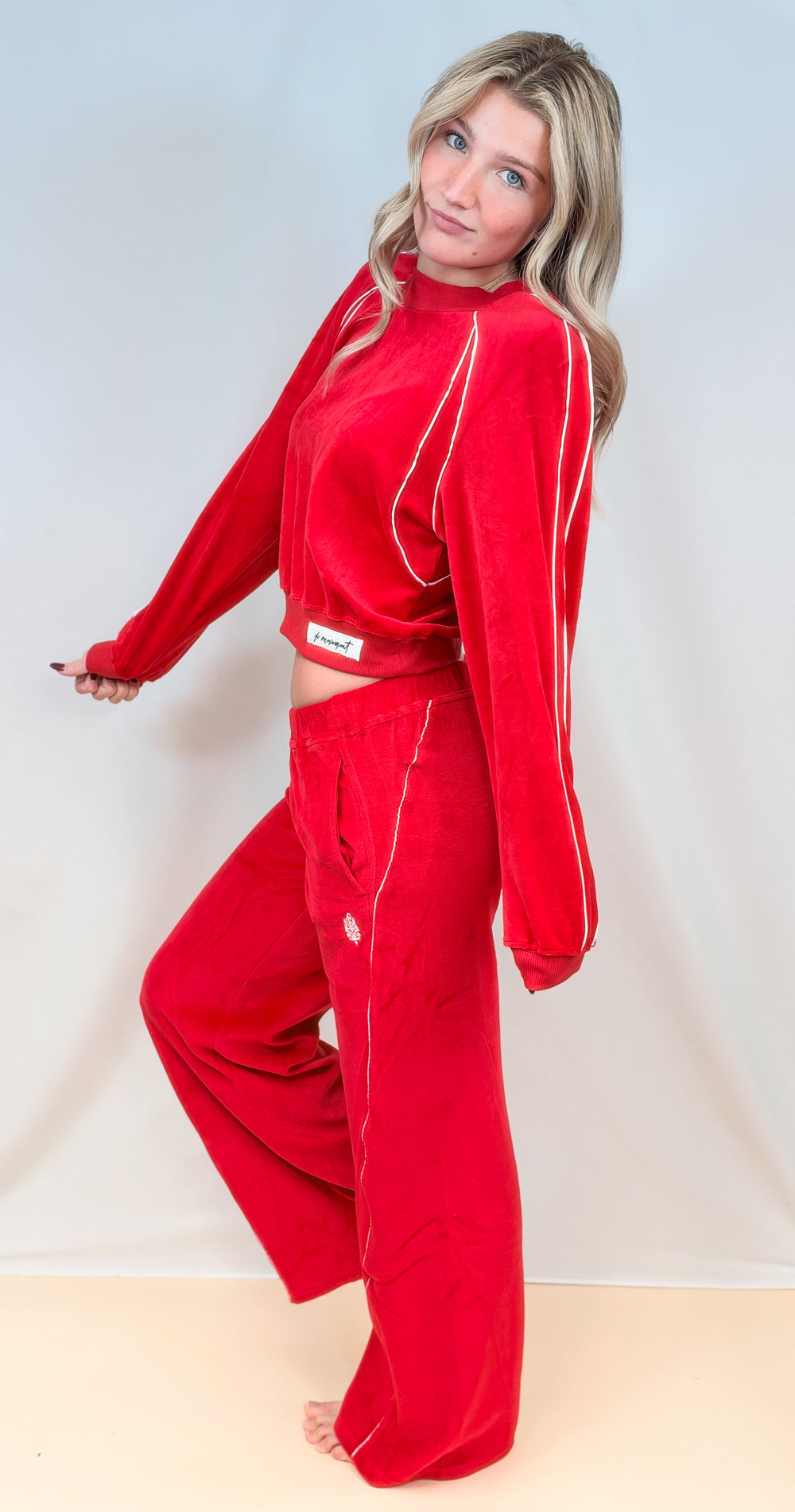 Woman shown from side view wearing matching red velour set with white piping on plain background