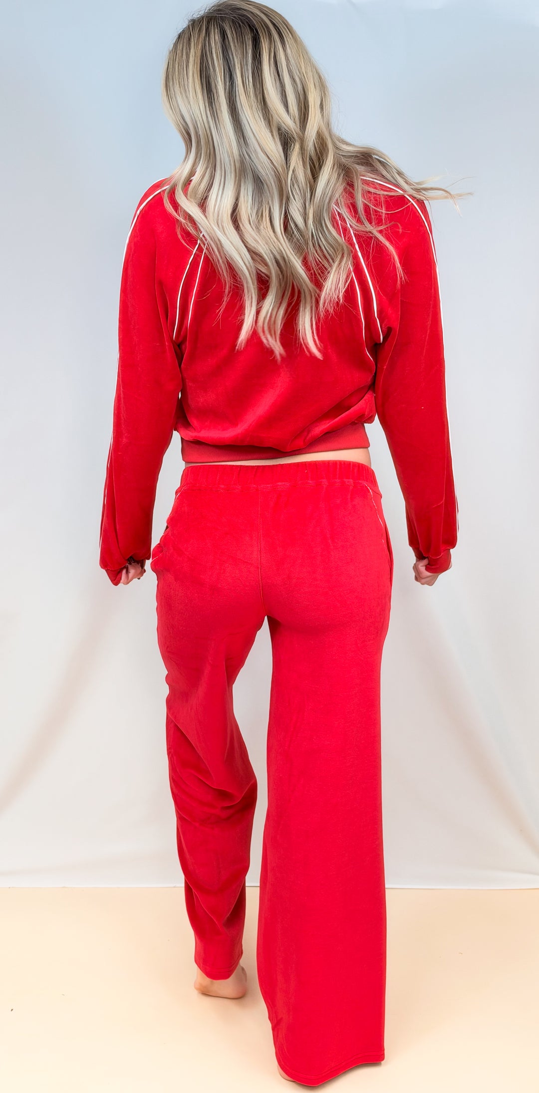 Woman shown from back view wearing matching red velour set with white piping on plain background