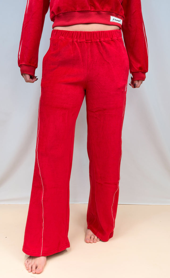 Woman shown waist down wearing red velour pants on plain background