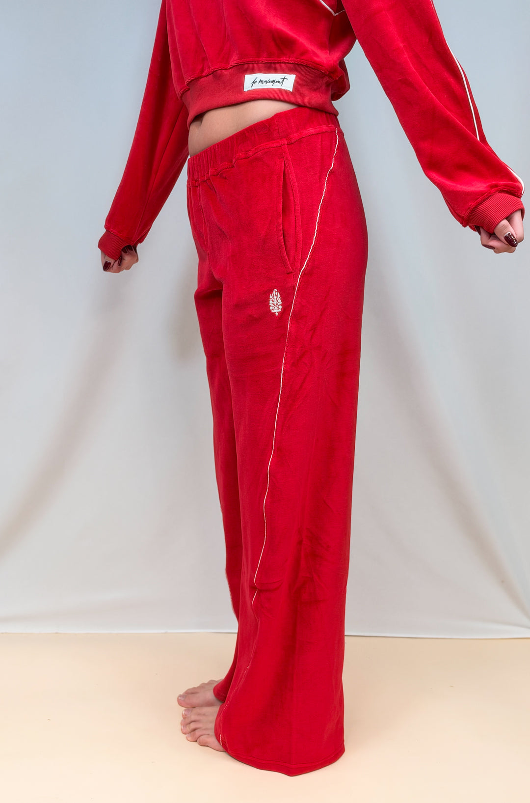 Woman shown from side view wearing red velour pants with white piping on plain background