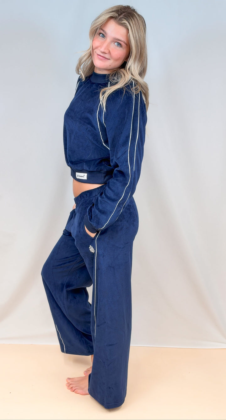Woman shown from side view wearing matching blue velour set with white piping on plain background