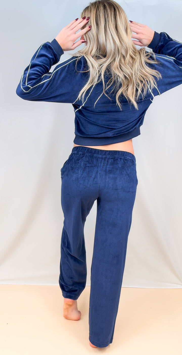Woman shown from back view wearing matching blue velour set with white piping on plain background