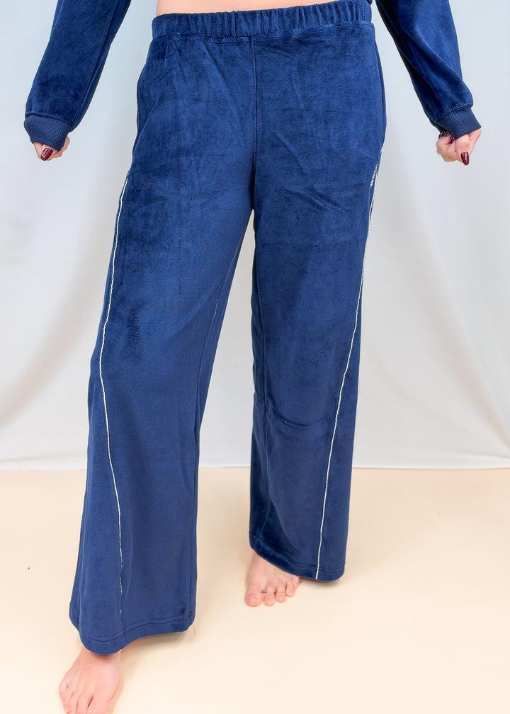 Woman shown waist down wearing blue velour pants with white piping on plain background